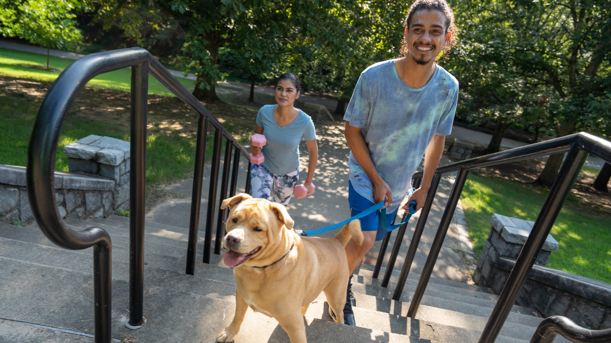 Two adults walking up stairs with a dog on a leash.