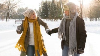 Two people walking in the snow wearing scarves and jackets.