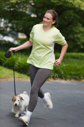A woman jogging in a park with her dog.