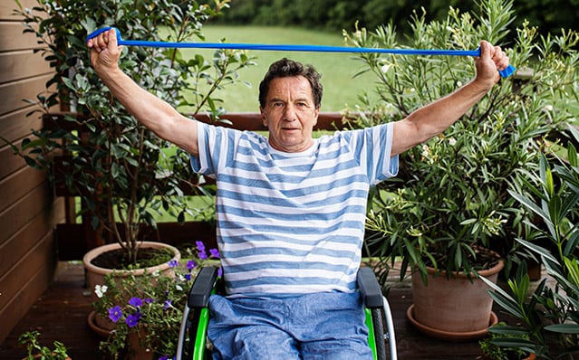 Un hombre mayor en silla de ruedas haciendo ejercicio en la terraza.
