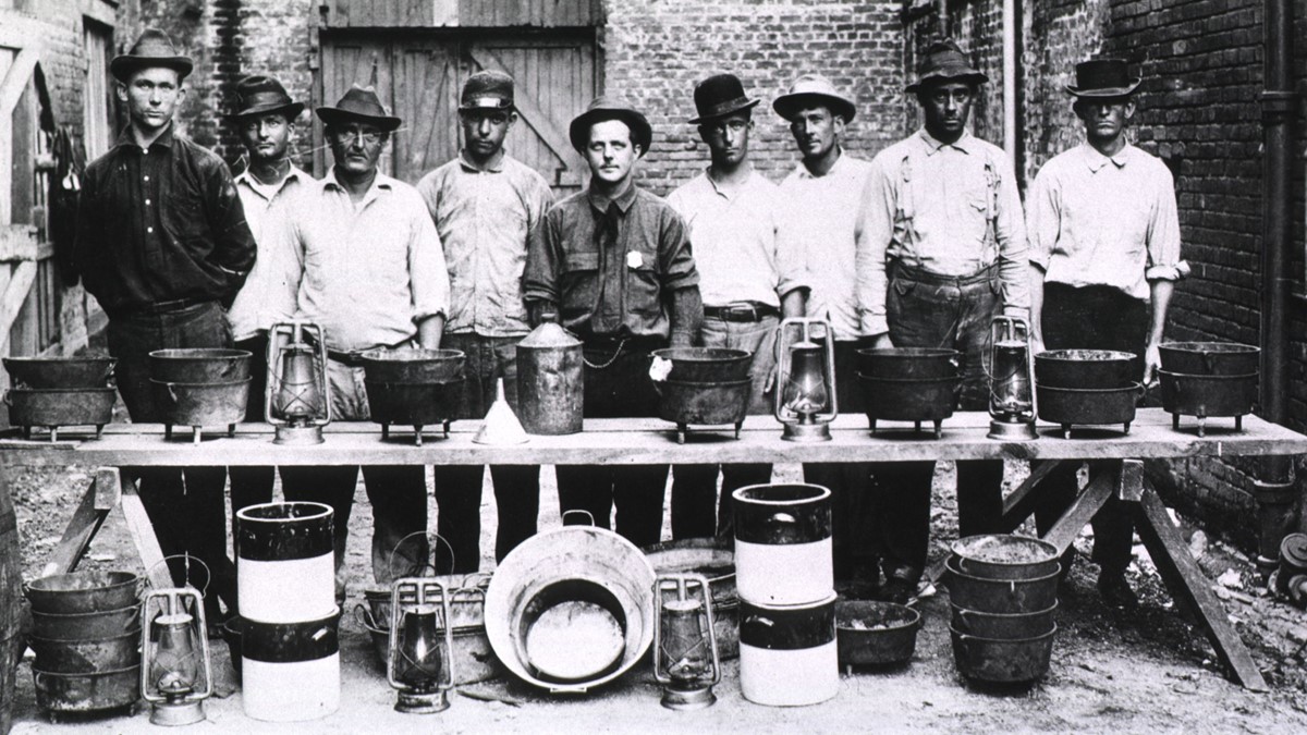 Rat Catchers in New Orleans; Group portrait of nine men standing behind a makeshift table