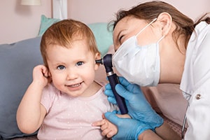 Pediatra revisa el oído de una bebé con otoscopio para el examen de otorrinolanringología (ojos, oídos y garganta) en casa