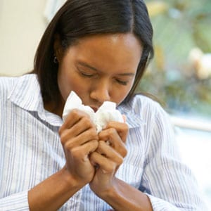 A sick young woman sneezing into a tissue