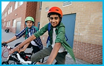 Two young boys sit on bikes outside of a school building.