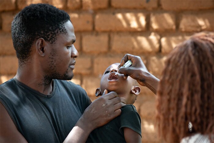 A father holds his daughter as she receives the Oral Polio Vaccine in Malawi.