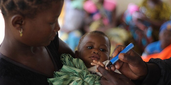 A mother holds her child, whose finger is being marked to show that the child received a polio vaccine.