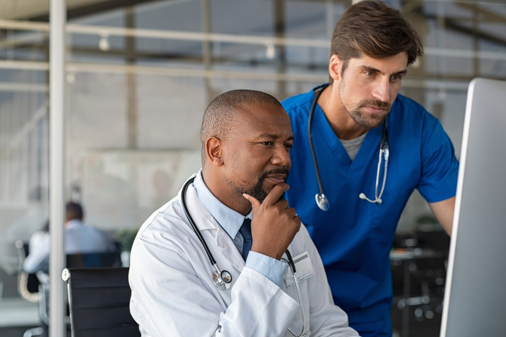 Male healthcare providers discuss a patient while looking at a computer.