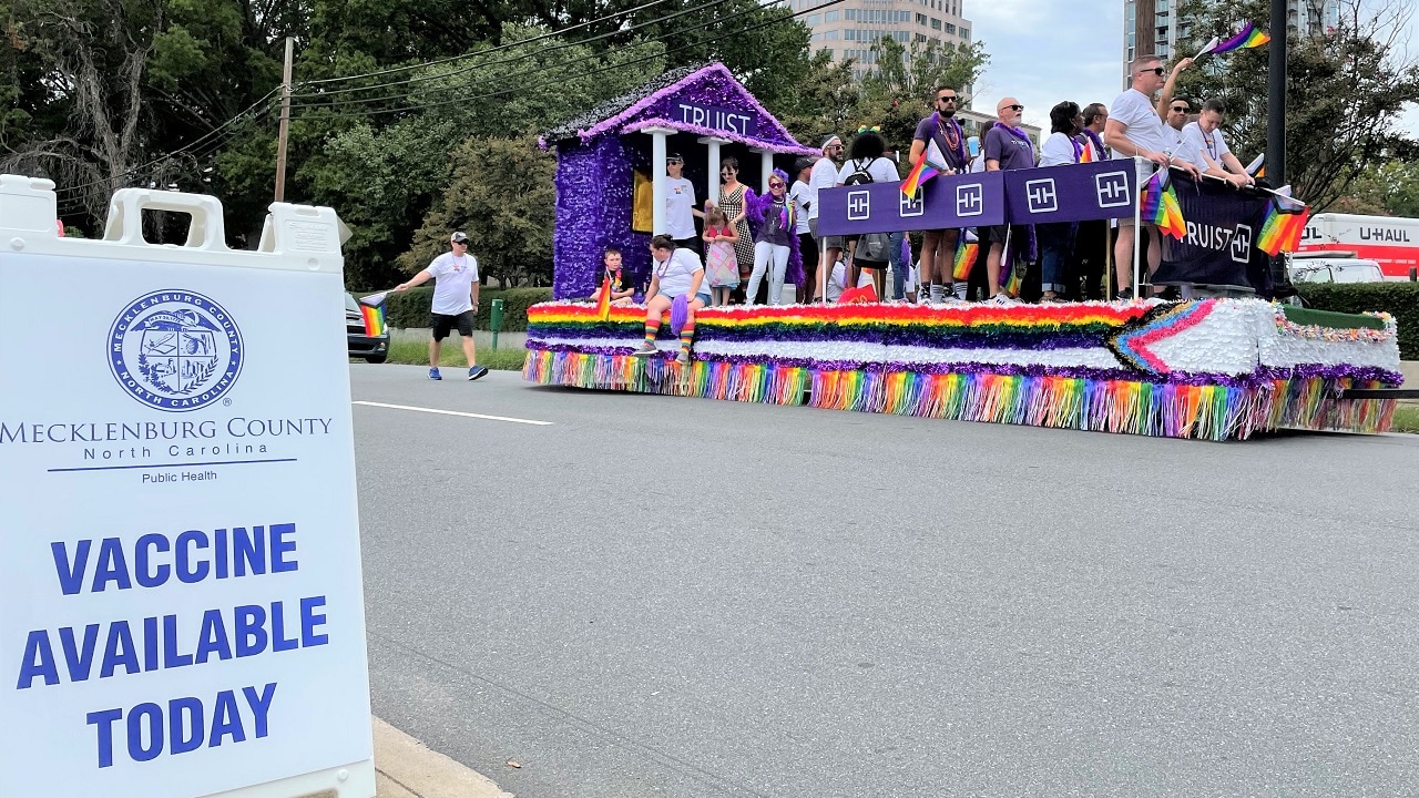 Charlotte Pride Parade participants ride past a sign offering monkeypox vaccine to event attendees.