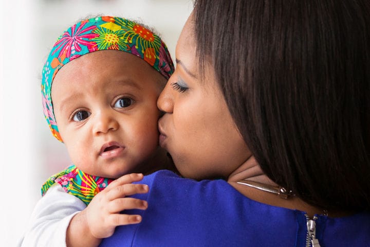A woman holding the baby and kissing it on the cheek.