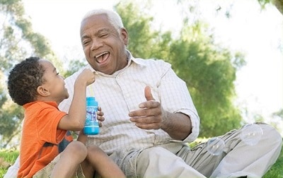 Young boy and grandfather blowing bubbles outside