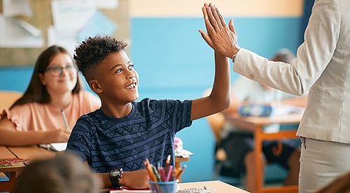 Black male student receives teacher high-five with female student in the background.