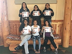 six teen girls, sitting and standing, holding up certificates of completion and smiling