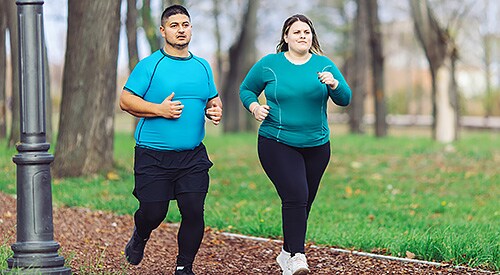 Young Hispanic man and young White woman jogging through a park.