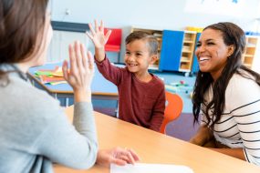Preschool teacher gives smiling boy a high five