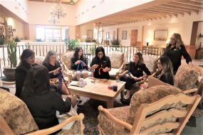 group of diverse women sit in a circle participating in a team building exercise.