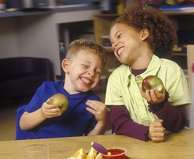 Two children laughing and eating apples