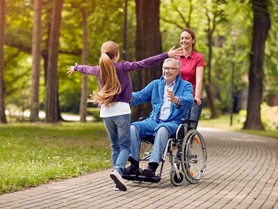 An adolescent girl is running with open arms toward a man in wheelchair.