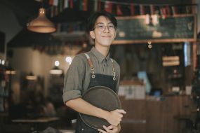 asian teenage boy waiter looking at camera smiling work at cafe opening