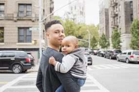 Young father walking with infant daughter in city neighborhood