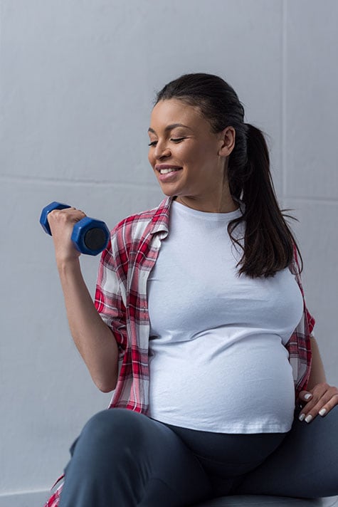 Happy African american pregnant woman exercising with dumbbells