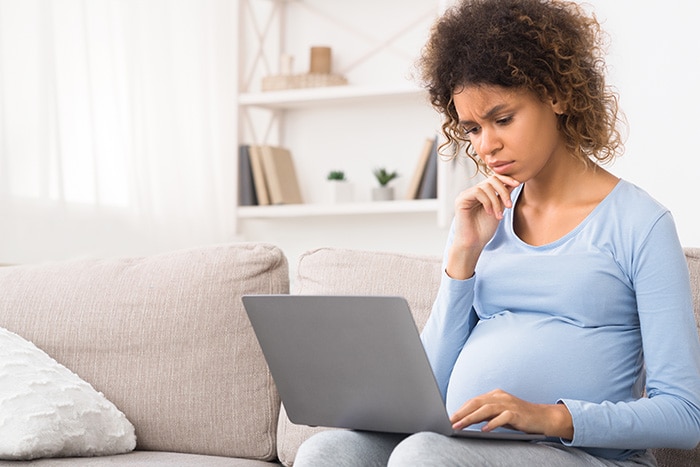 Pregnant woman on couch reading on her laptop computer