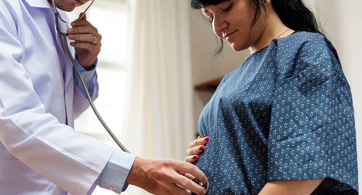Doctor listening to pregnant woman's baby with stethoscope
