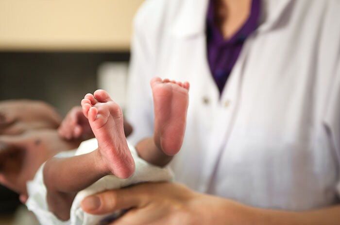 Doctor is holding tiny baby, feet are visible.