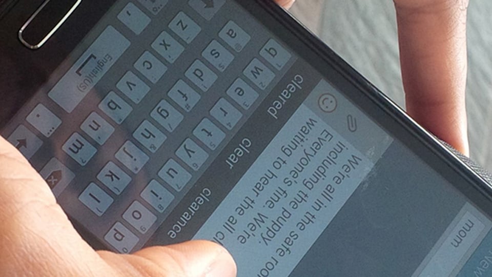 Close-up of hands using a smart phone typing a message on the screen keyboard.