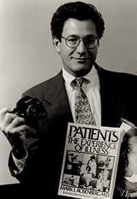 Mark L Rosenberg holding camera and book.