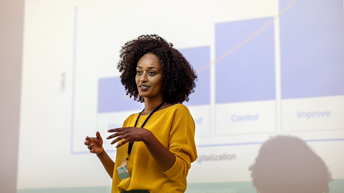 Woman standing and explaining chart on large screen behind her.