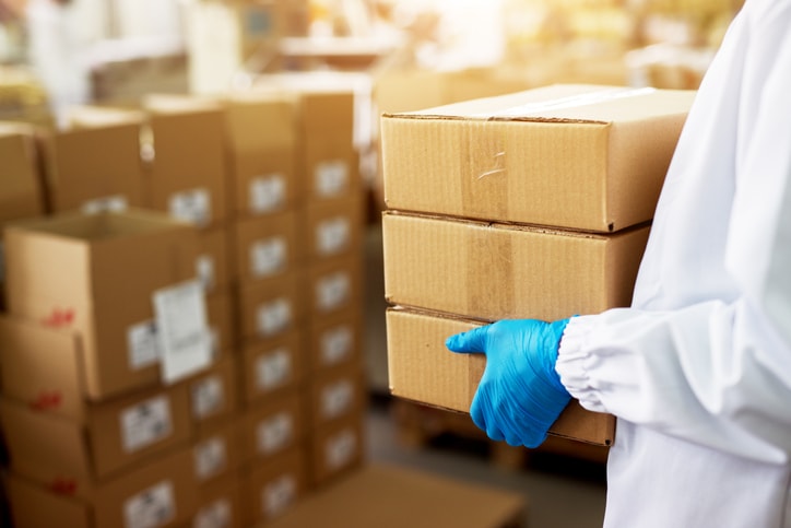 Image shows someone in a white coat and gloves holding boxes.