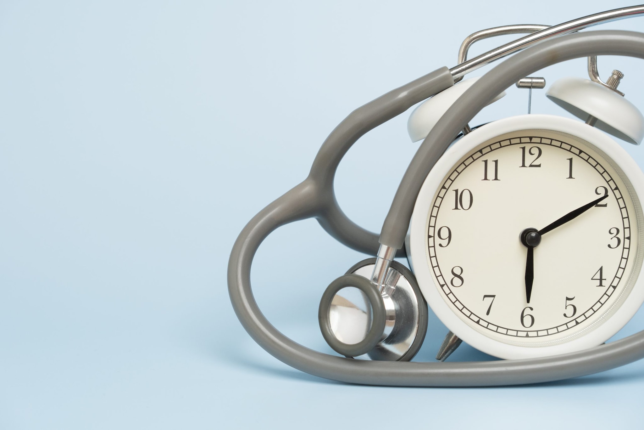 Close-up of a grey stethoscope draped over an analog alarm clock