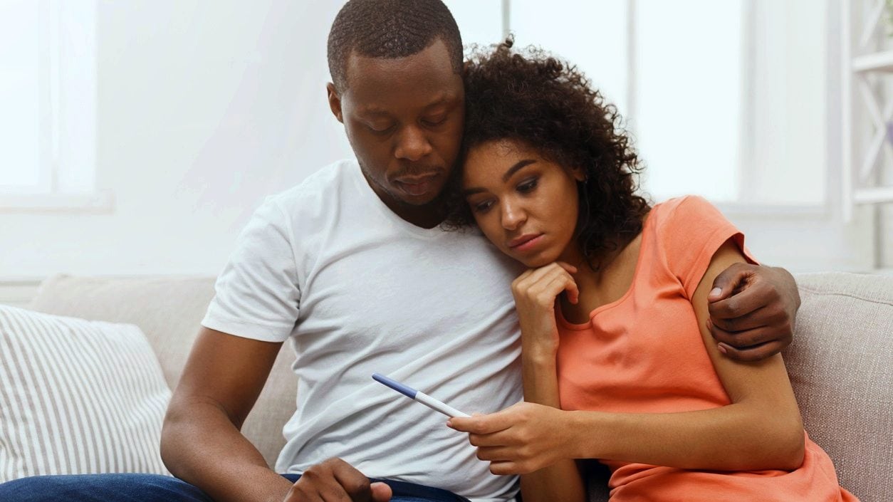 Couple holding each other looking down at a pregnancy test