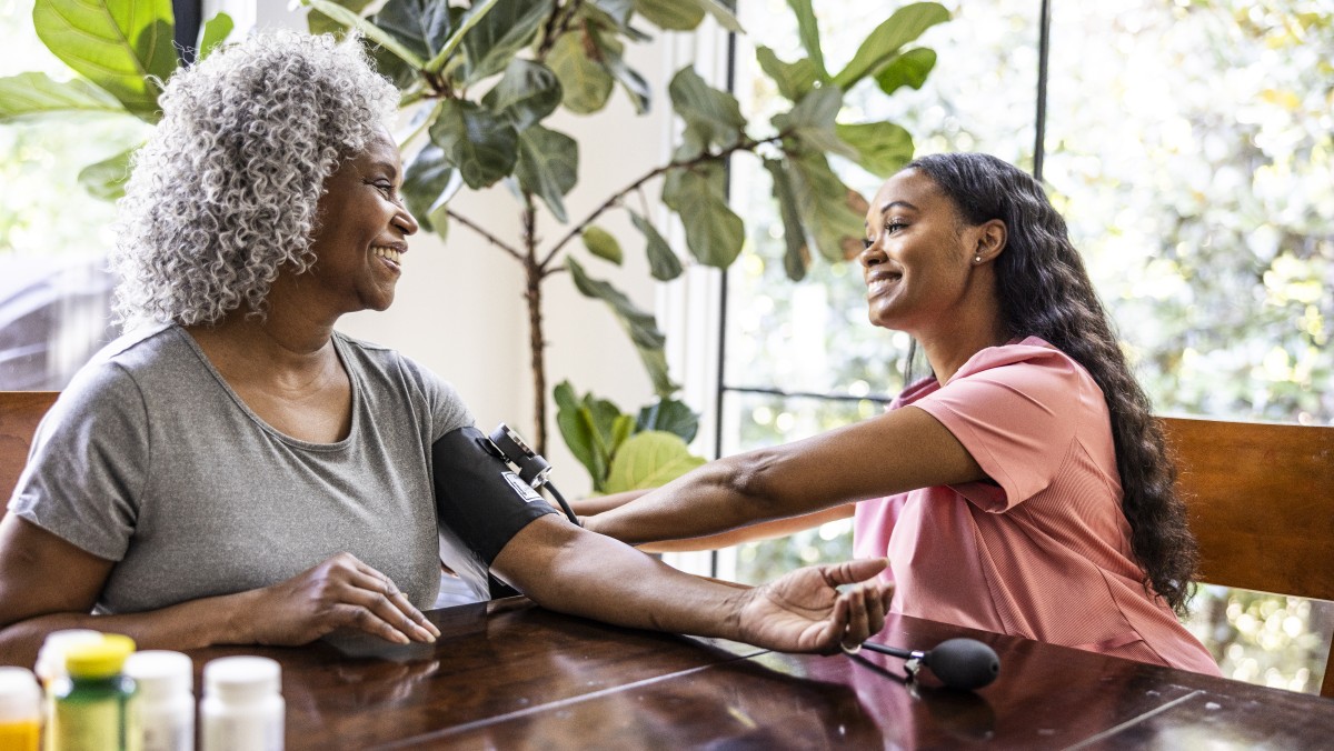 An older woman smiles at a healthcare provider during a blood pressure check.