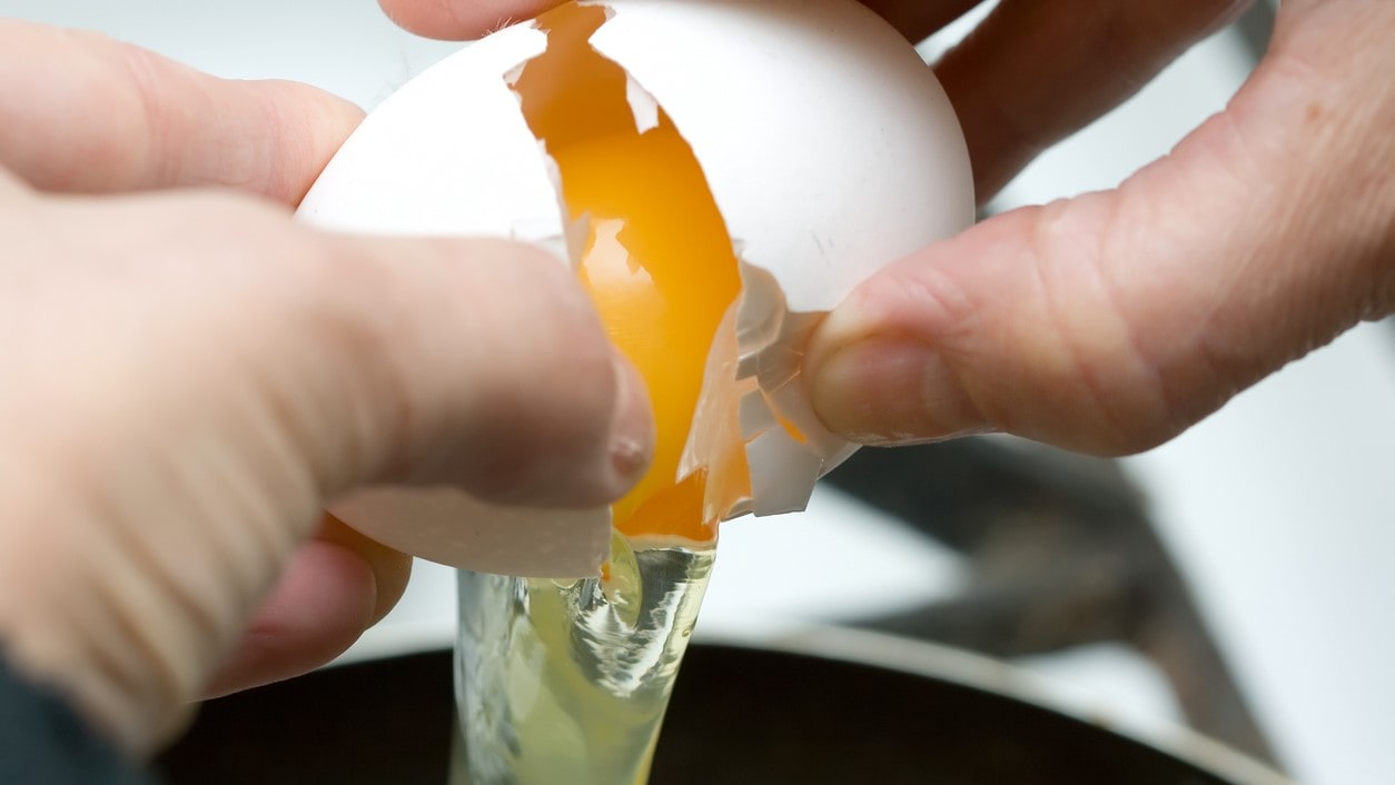 Hands cracking open an egg over a bowl.