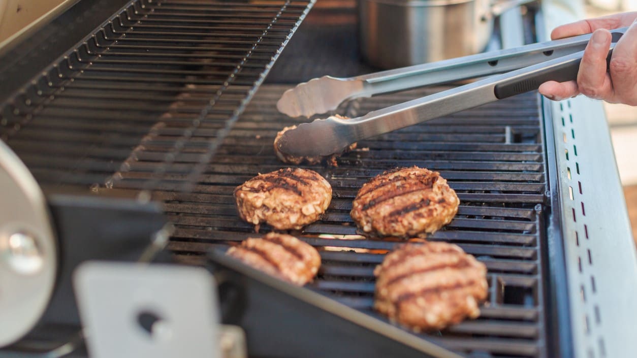 Grill with hamburger patties and a person holding tongs.