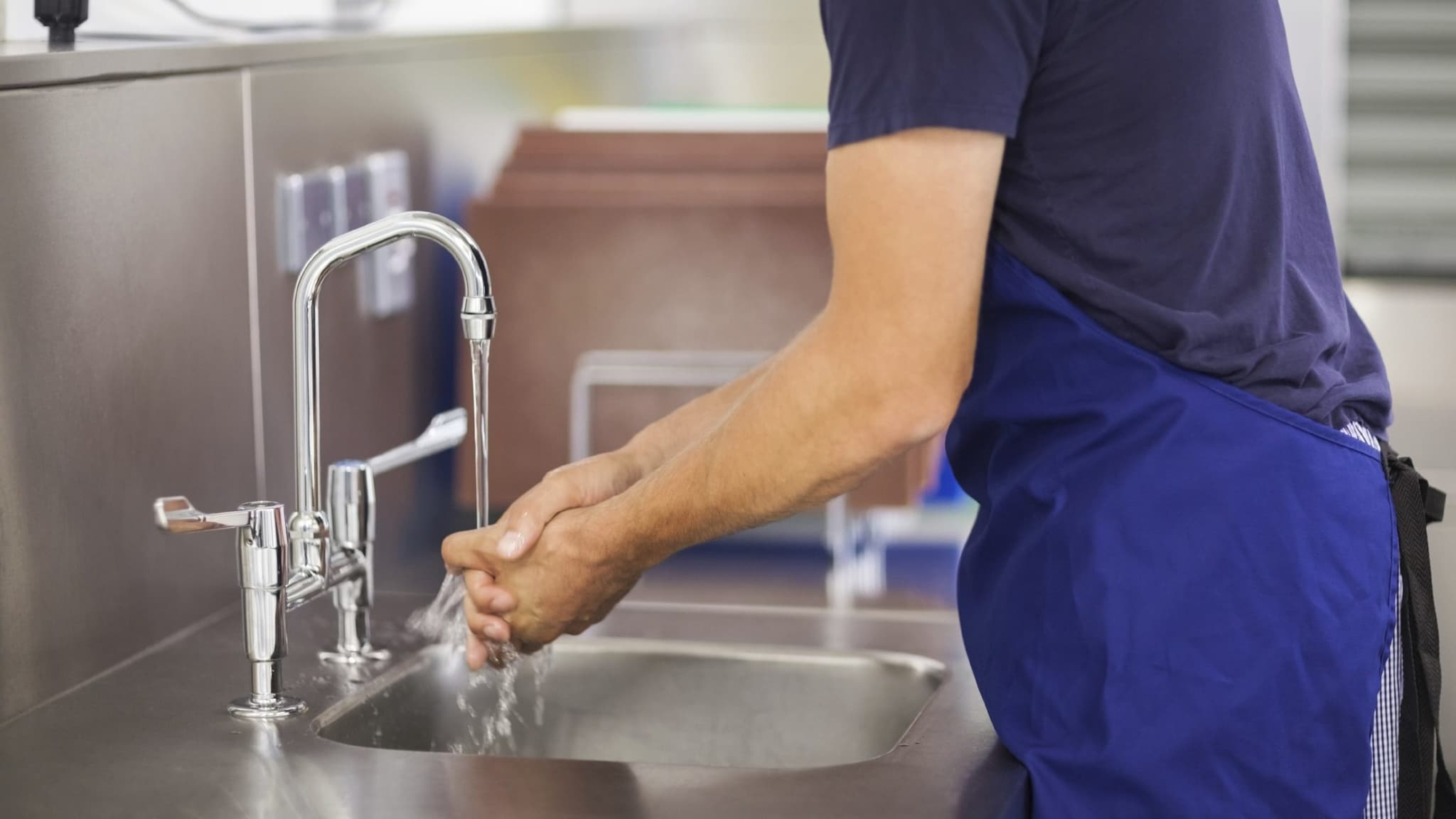 Person washing their hands at a restaurant kitchen sink.