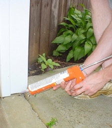 Person using caulk gun to seal holes on exterior of house