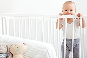 Infant standing up in crib teething on crib rail