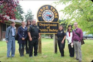 A group of people stand near the sign for the Yurok tribe.