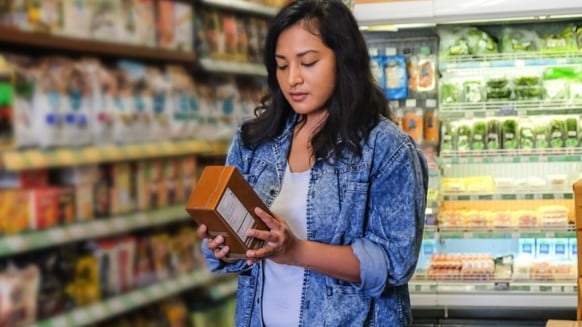 A woman reading the nutrition label on a package in a grocery store.