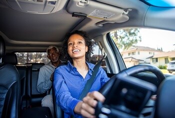 Photo of a ride-sharing service: a young African-American woman is driving, and a mature African-American man is a passenger.