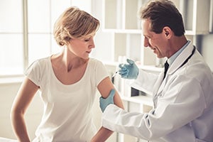 doctor injecting vaccine dose in woman’s arm muscle.