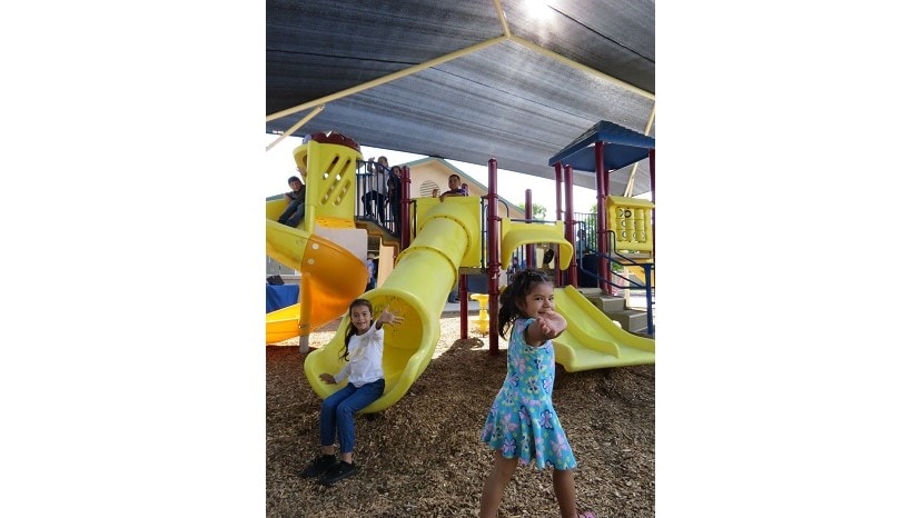 Foto de niños jugando bajo una estructura que les proporciona sombra, financiada por la Academia Estadounidense de Dermatología.