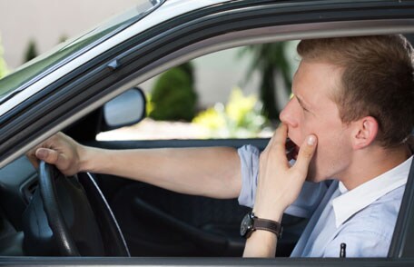 Man yawning behind wheel of car
