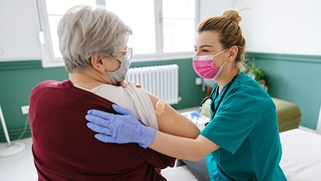 Una enfermera asistiendo a una paciente y las dos con mascarillas