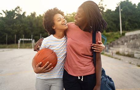 Una madre y su hijo abrazándose mientras uno sostiene una pelota de baloncesto.