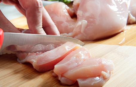 Unas manos cortando pollo crudo con un cuchillo.