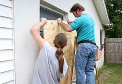 Dos personas clavando una tabla de madera para cubrir una ventana   