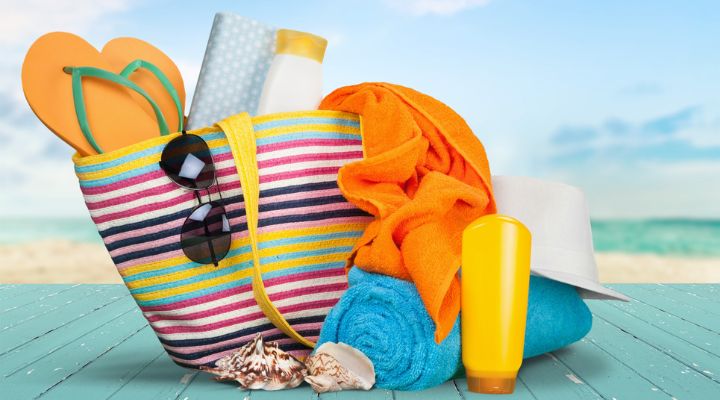 Un bolso de mano con unas sandalias, gafas del sol, protector solar, toallas, y un sombrero.
